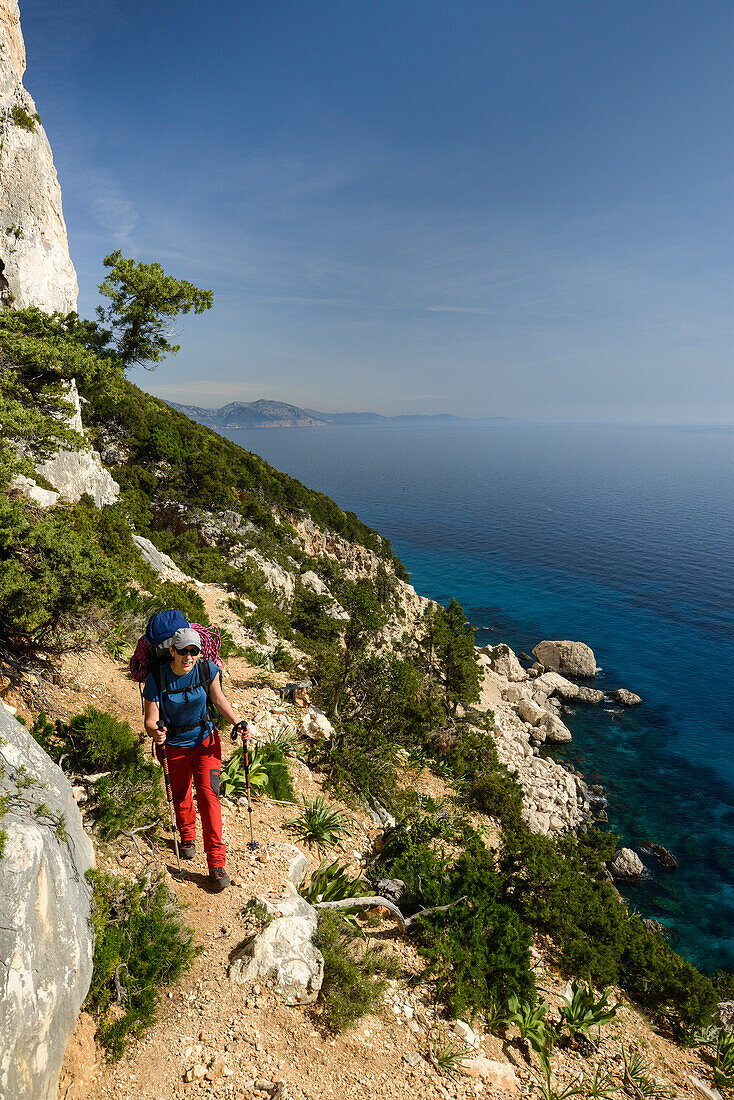 Eine junge Frau mit Trekkingausrüstung wandert oberhalb des Meeres entlang der gebirgigen Küste, Golfo di Orosei, Selvaggio Blu, Sardinien, Italien, Europa