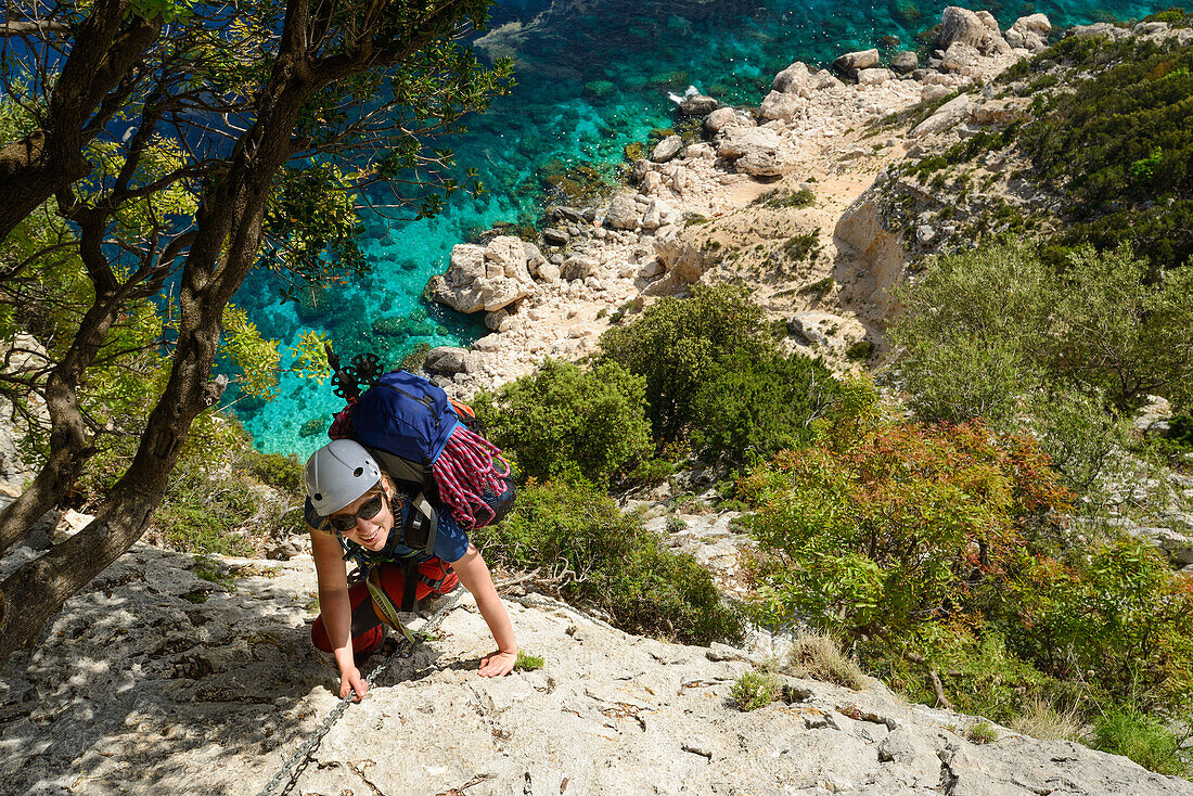 Frau klettert eine steile Wand über dem Meer mit Kette versichert hinauf, Selvaggio Blu, Golfo di Orosei, Sardinien, Italien, Europa