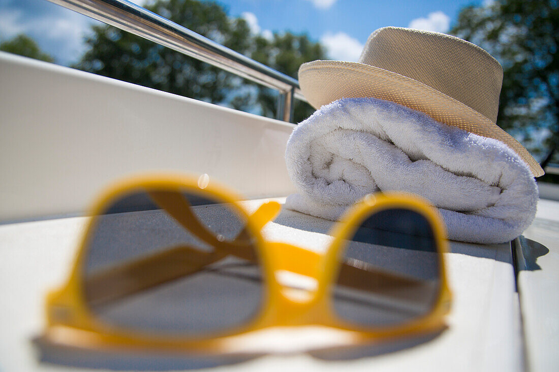 Stillleben mit gelber Sonnenbrille, Hut und Handtuch an Deck von einem Le Boat Royal Mystique Hausboot auf dem Kanal Plassendale - Niuewpoort, Flander, Belgien