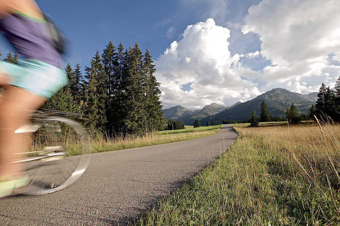 Junge Frau fährt mit ihrem Fahrrad in der Nähe der Berge an einem sonnigen Tag, Tannheimer Tal, Tirol, Österreich