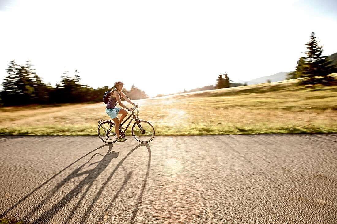 Young woman riding her bike near a meadow on a sunny day, Tannheimer Tal, Tyrol, Austria