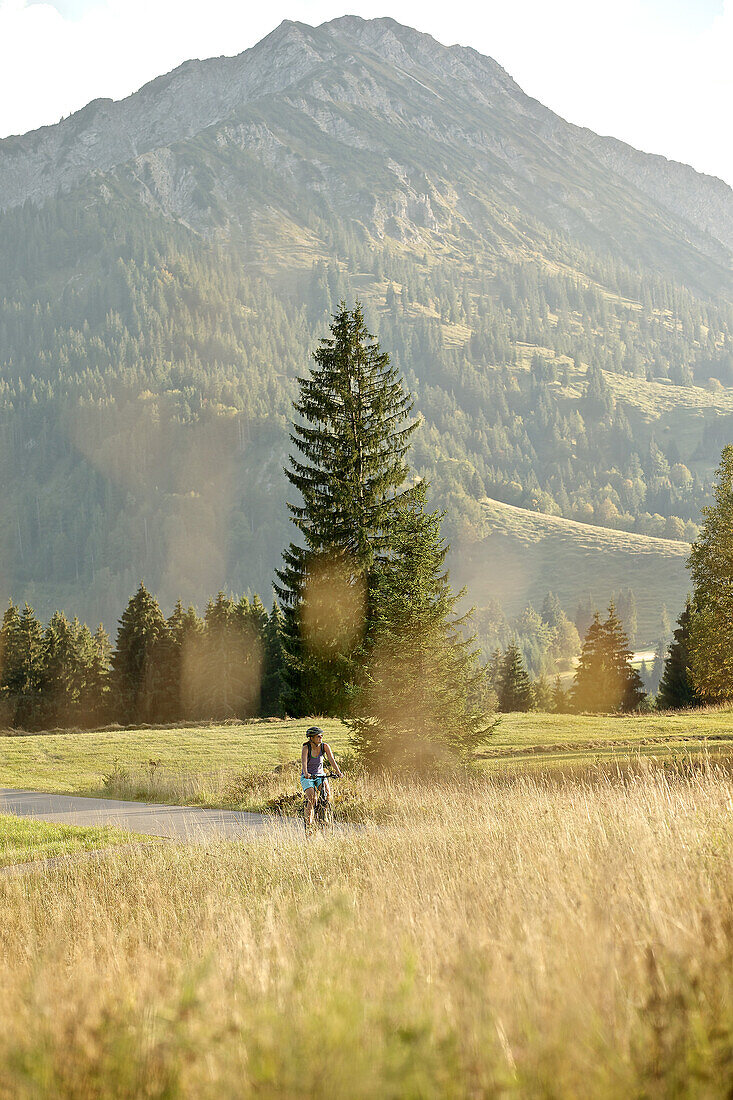 Junge Frau fährt mit ihrem Fahrad in der Nähe der Berge an einem sonnigen Tag, Tannheimer Tal, Tirol, Österreich