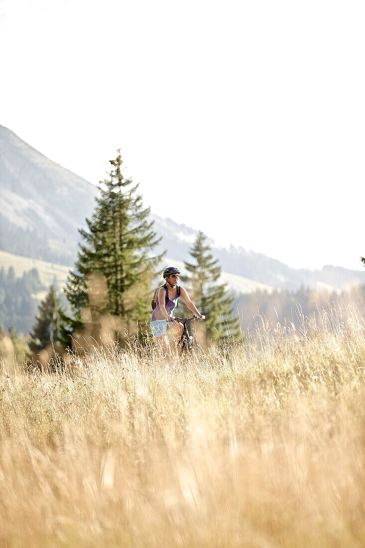 Young woman riding her bike near a meadow on a sunny day, Tannheimer Tal, Tyrol, Austria