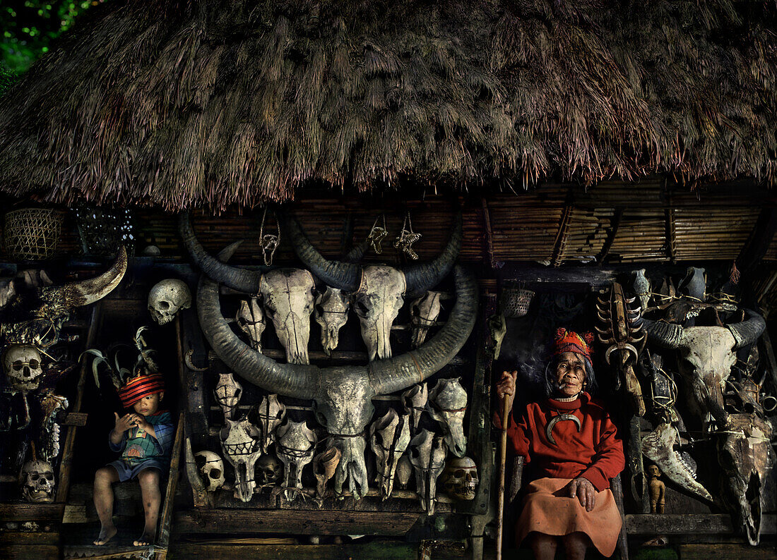 Old woman and boy in front of a hut with straw roof and buffalo skulls, Ifugao, Luzon, Philippines, Asia