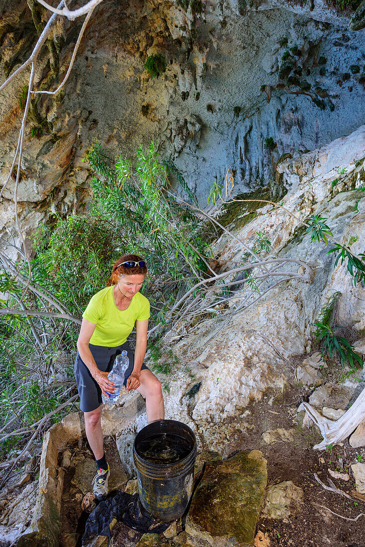 Frau steht in Halbhöhle vor Tropfwasserfass, Selvaggio Blu, Nationalpark Golfo di Orosei e del Gennargentu, Sardinien, Italien