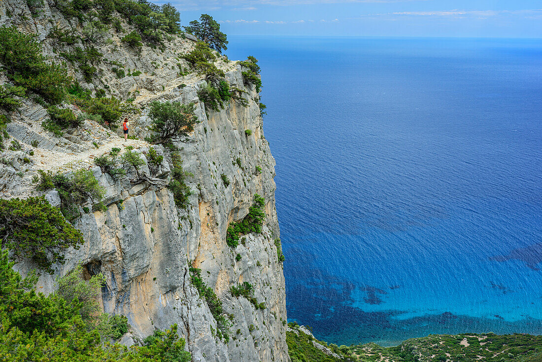 Frau wandert am Selvaggio Blu über Felsabbruch entlang, Selvaggio Blu, Nationalpark Golfo di Orosei e del Gennargentu, Sardinien, Italien