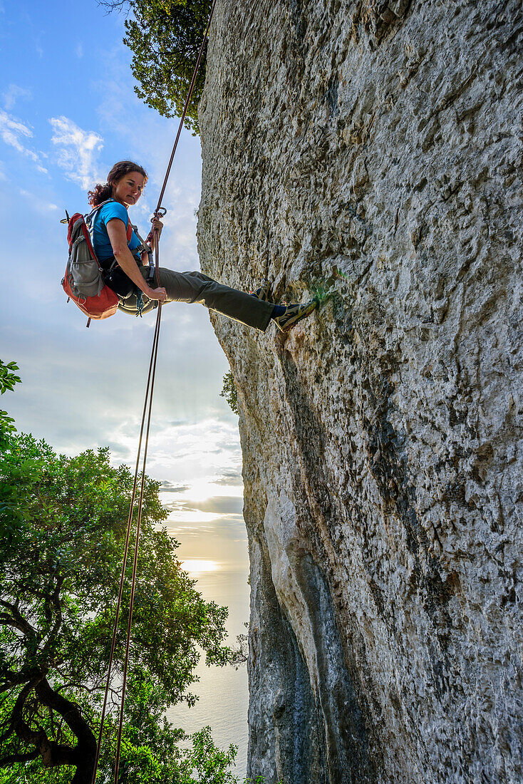 Woman rapelling over rockface, Mediterranean in background, Selvaggio Blu, National Park of the Bay of Orosei and Gennargentu, Sardinia, Italy