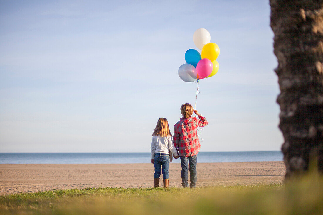 Brother and sister at the beach in winter with balloons