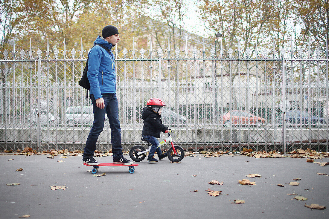 A 3 years old little boy on bike going with his father on skateboarding, in the streets of Paris