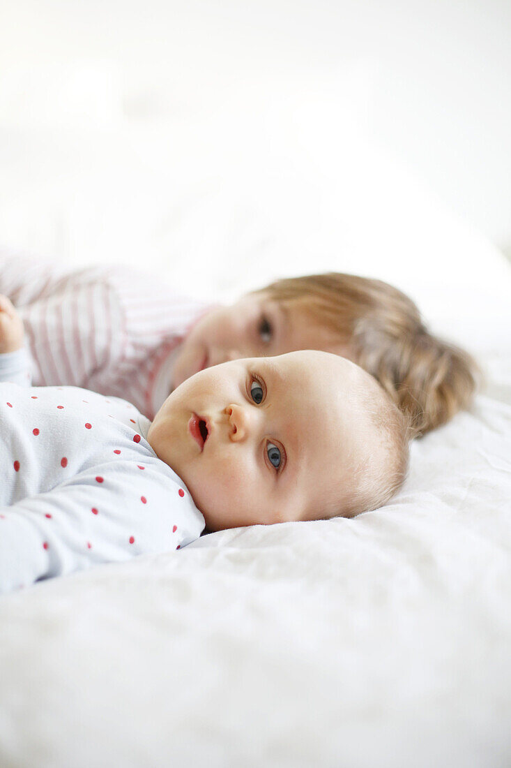 A little boy of 4 years hold and his baby sister of 10 months lying on a bed