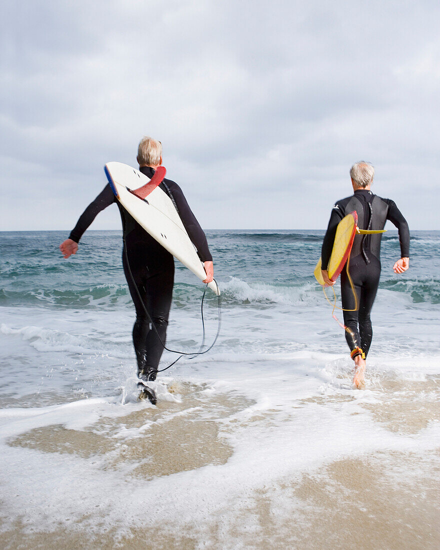 Two men walking into ocean with surfboards