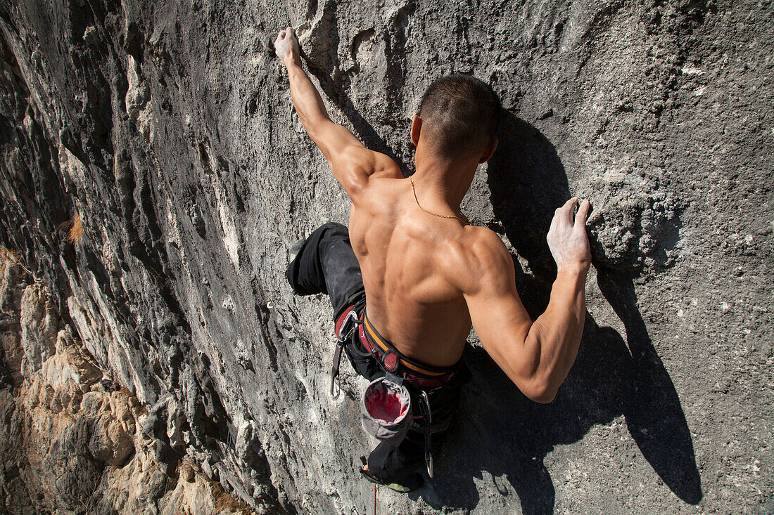 Asian climber scaling steep cliff face