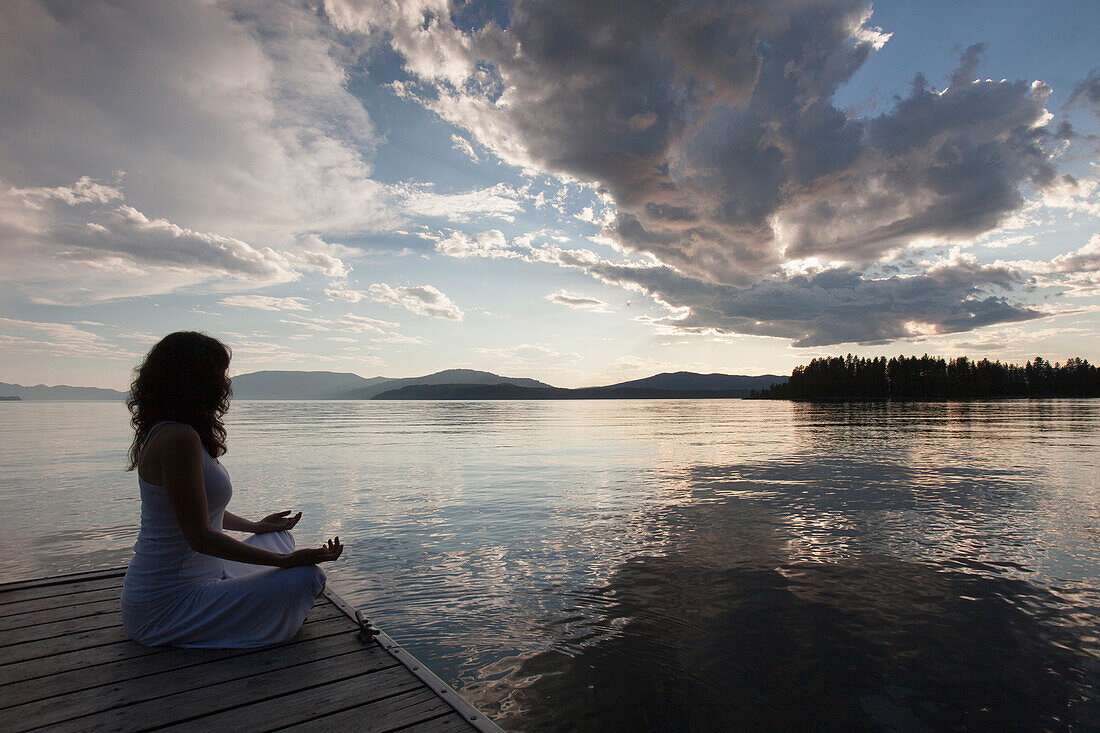 Caucasian woman meditating on wooden dock in still lake