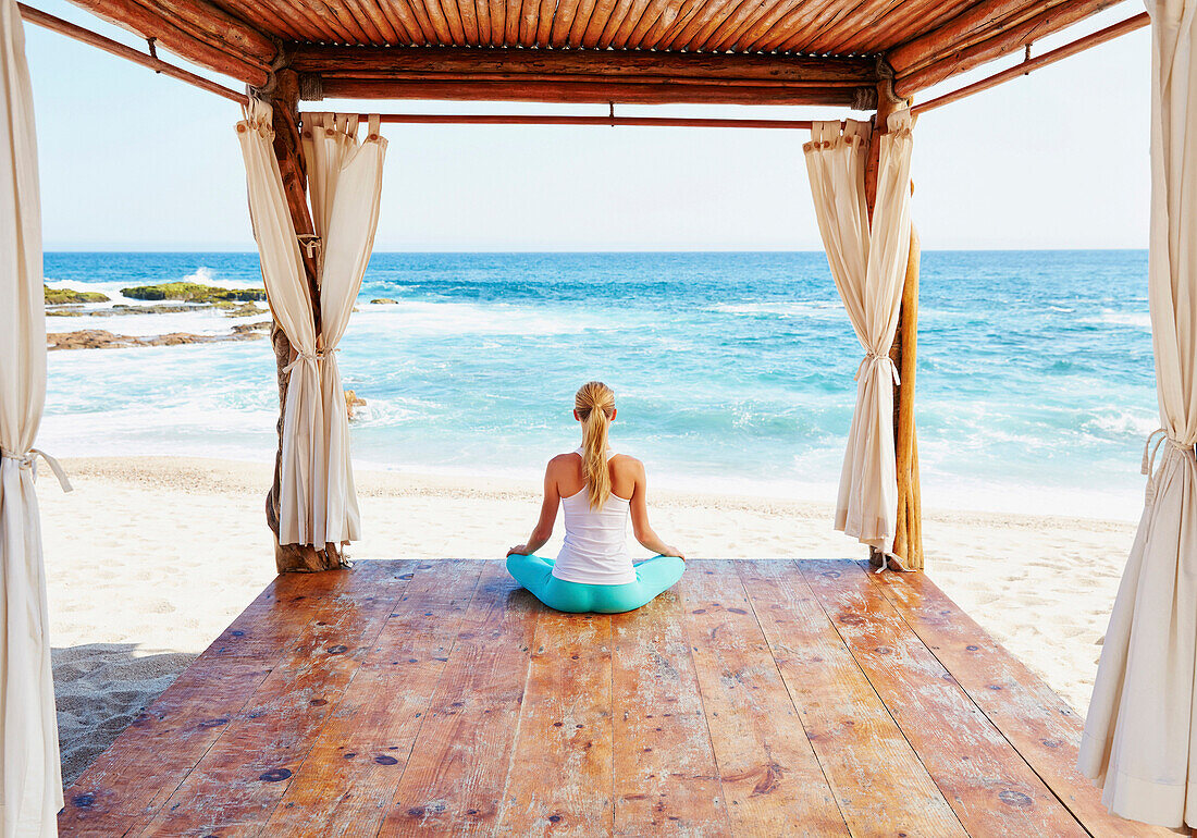 Caucasian woman meditating in cabana overlooking ocean