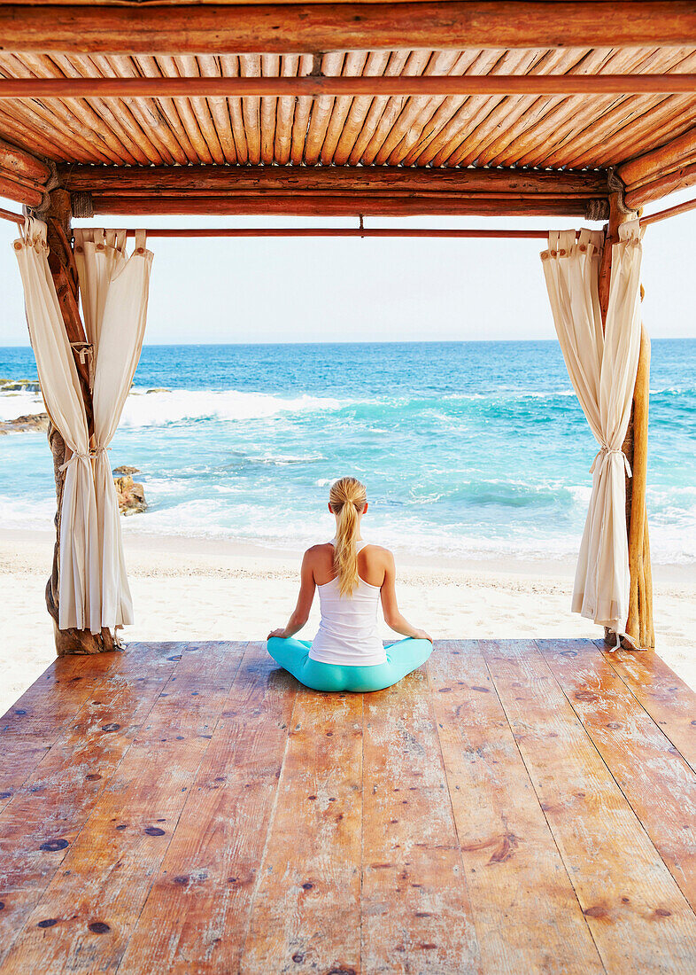 Caucasian woman meditating in cabana overlooking ocean