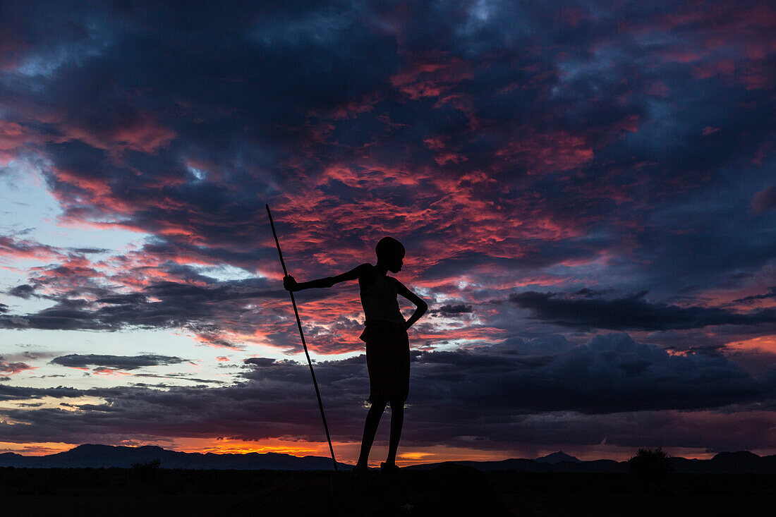 Silhouette of boy with walking stick under sunset sky, Nyangaton, Ethiopia