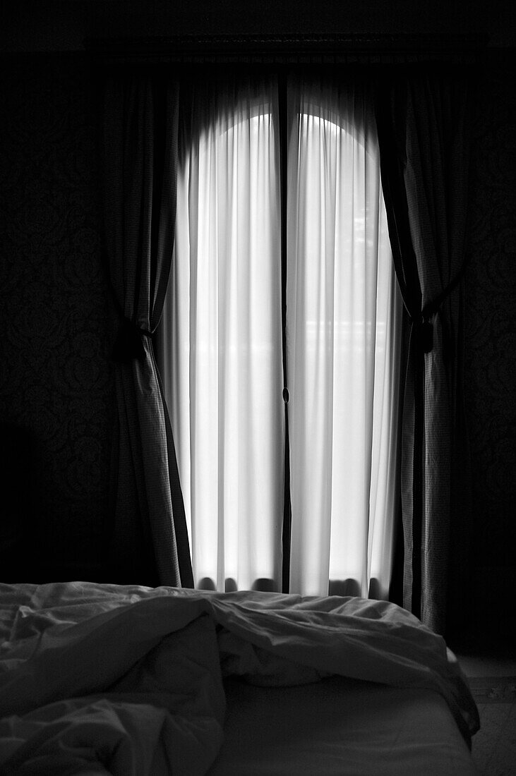 Sunlight Streaming Through Sheer Curtains of Hotel Room with Unmade Bed in Foreground