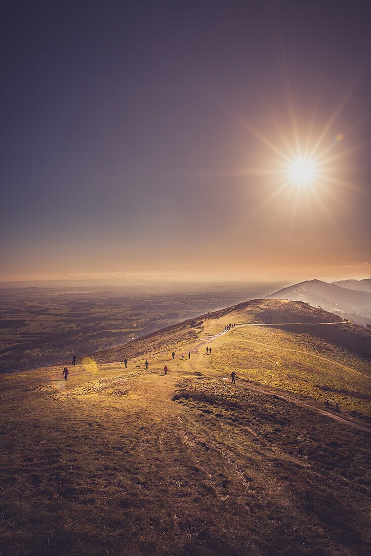 Group of People Walking Along Path atop Hill with Bright Sun