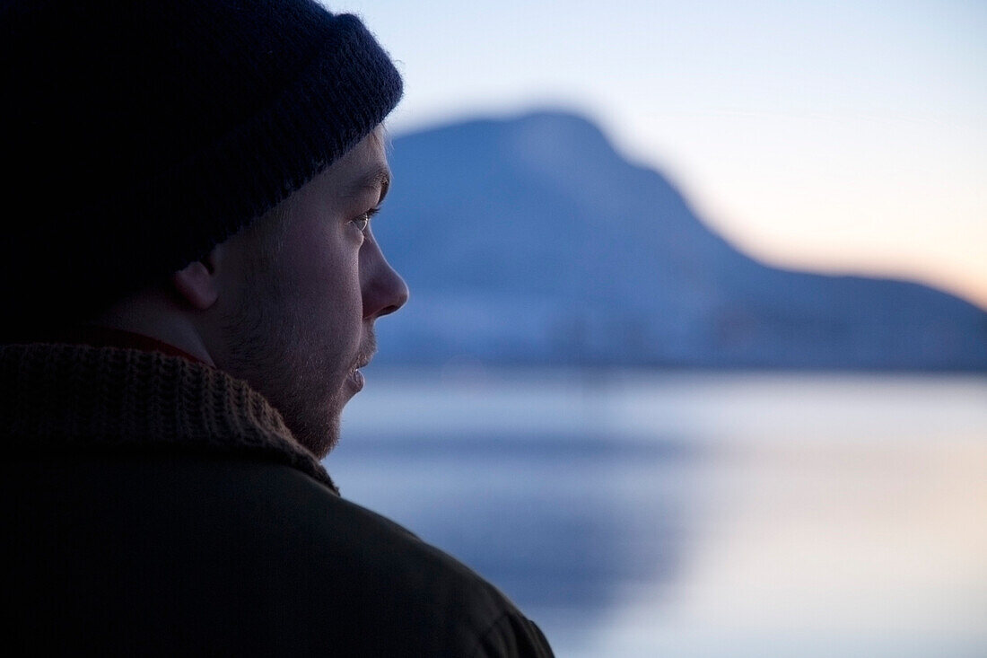Close-Up Portrait of Young Man Gazing at Winter Landscape at Dusk, Rear View
