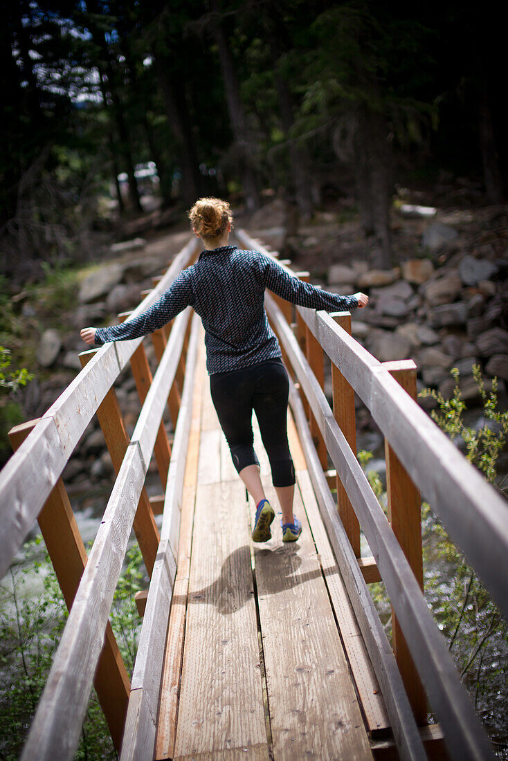 Young Woman Crossing Footbridge in Forest, Rear View