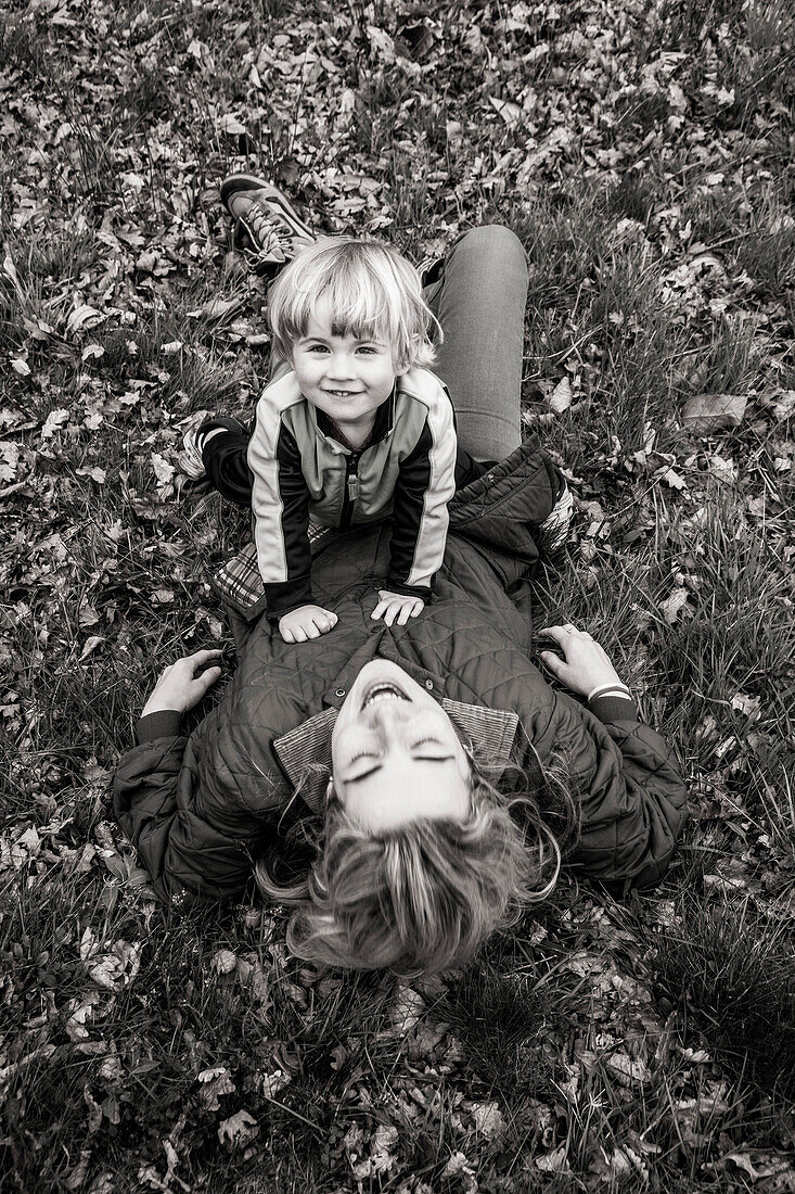 Smiling Young Son Sitting on Top of Mother Laying in Field, High Angle View