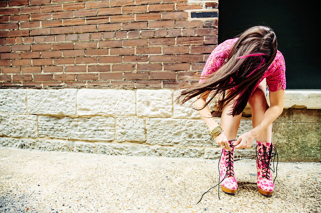 Caucasian woman tying boots on sidewalk, St Louis, MO, USA