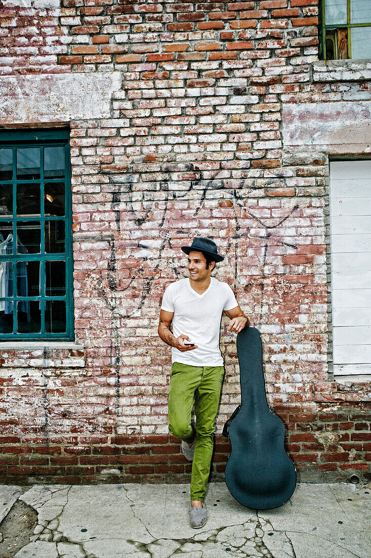 Mixed race musician with guitar case using cell phone, Los Angeles, California, USA
