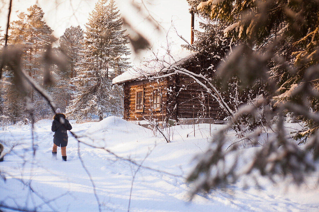 Caucasian woman walking near log cabin in snowy forest, C1