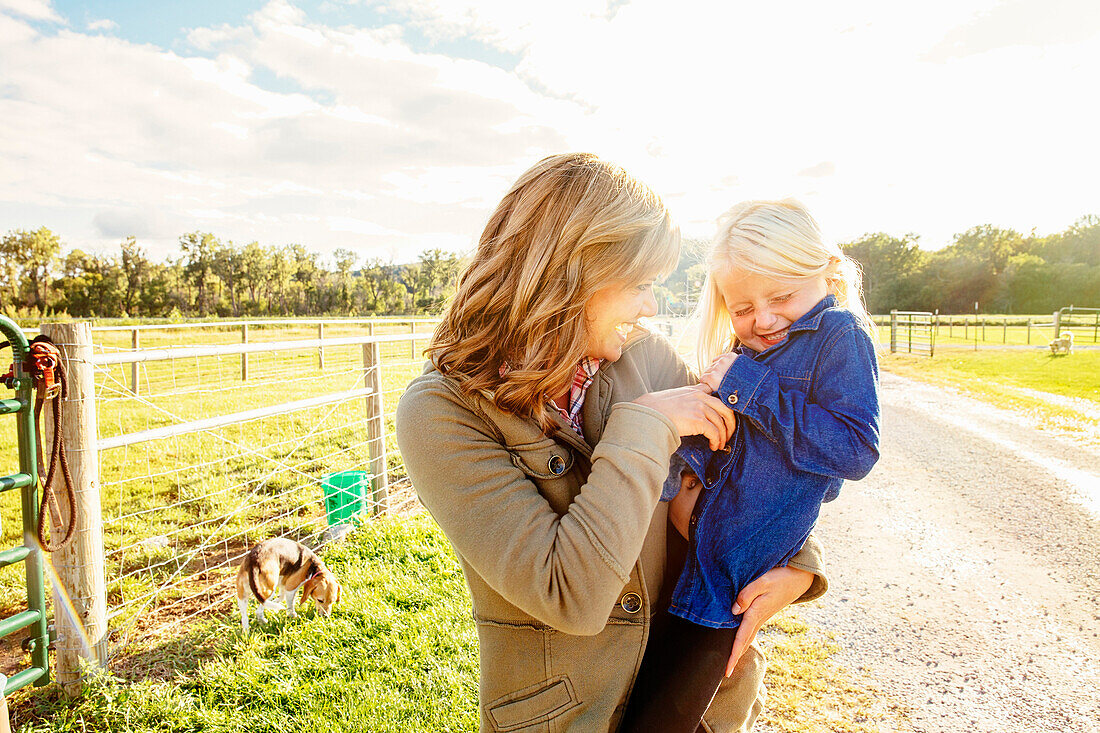 Caucasian mother tickling daughter on rural road, C1