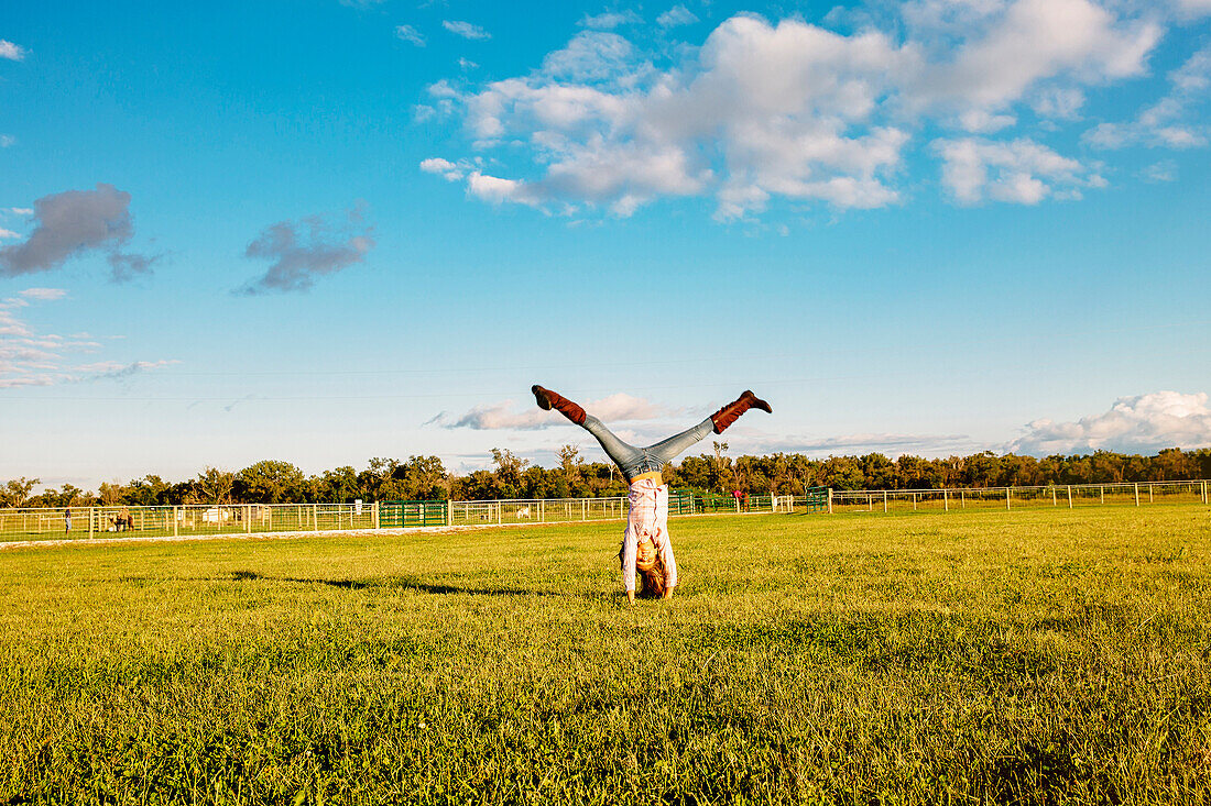 Caucasian girl doing headstand in field on ranch, C1
