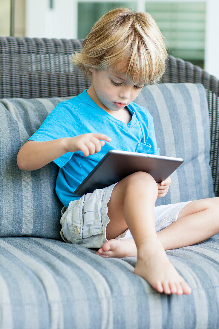 Caucasian boy using digital tablet on sofa, C1