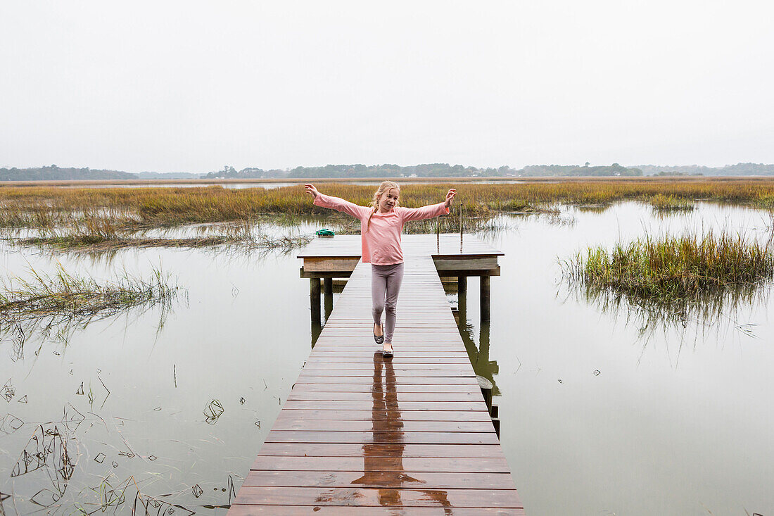 Caucasian girl standing on wooden dock over lake, C1