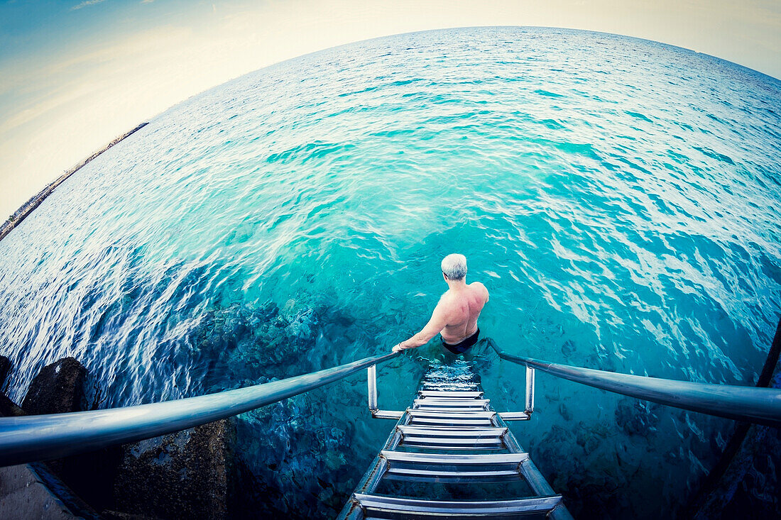Fish-eye lens view of older Caucasian man descending ladder into ocean, C1
