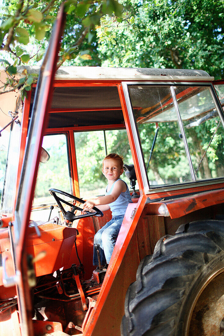Young boy driving a tractor in summer in the country