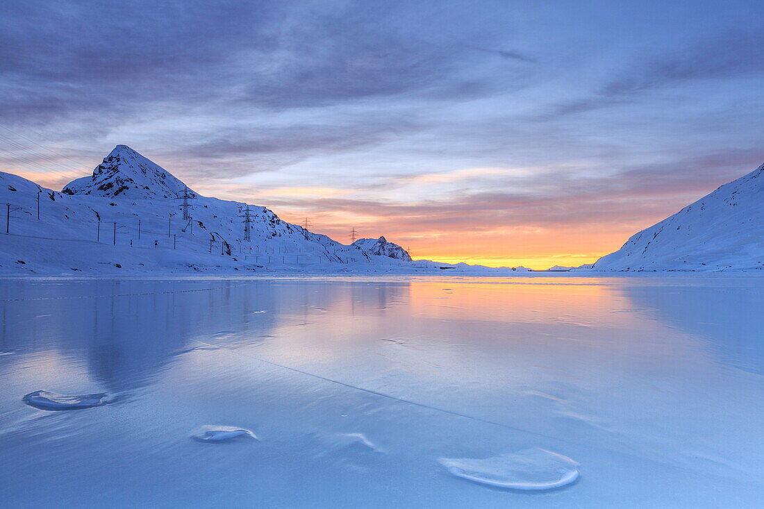 The colors of dawn invading the smooth surface of Lago Bianco exceptionally icy, Bernina Pass, Graubunden, Swiss Alps, Switzerland, Europe