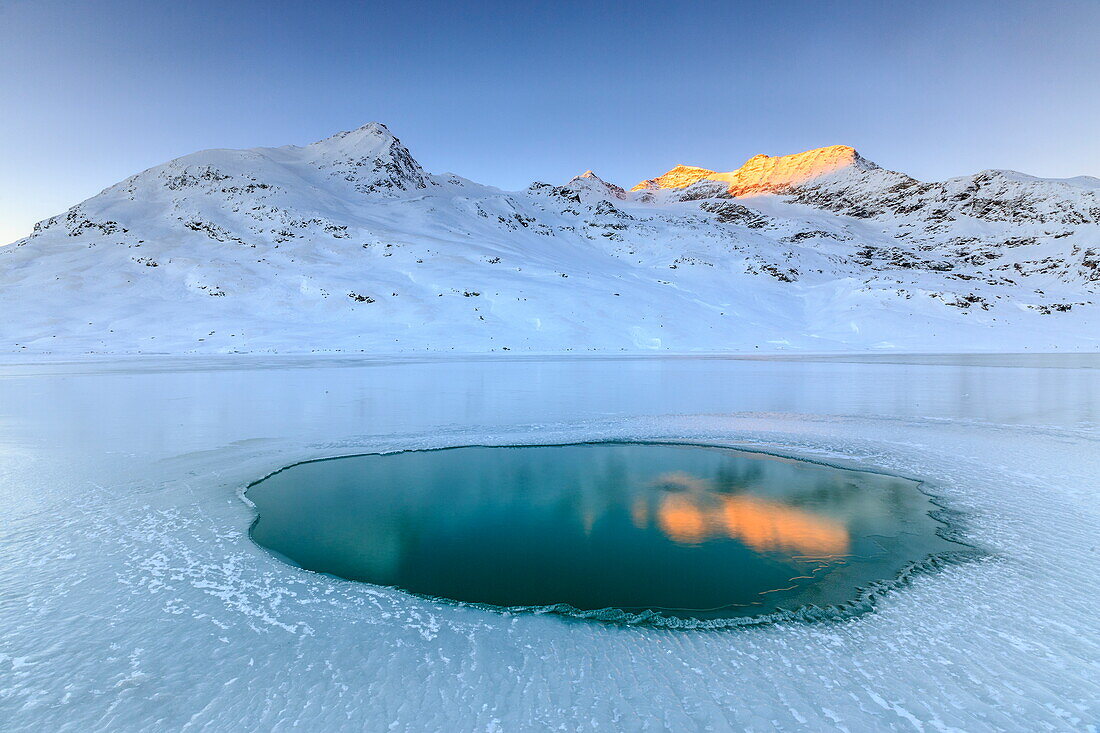 The Piz Cambrena illuminated by the sun reflecting in a pool surrounded by ice at the Bernina, Graubunden, Swiss Alps, Switzerland, Europe