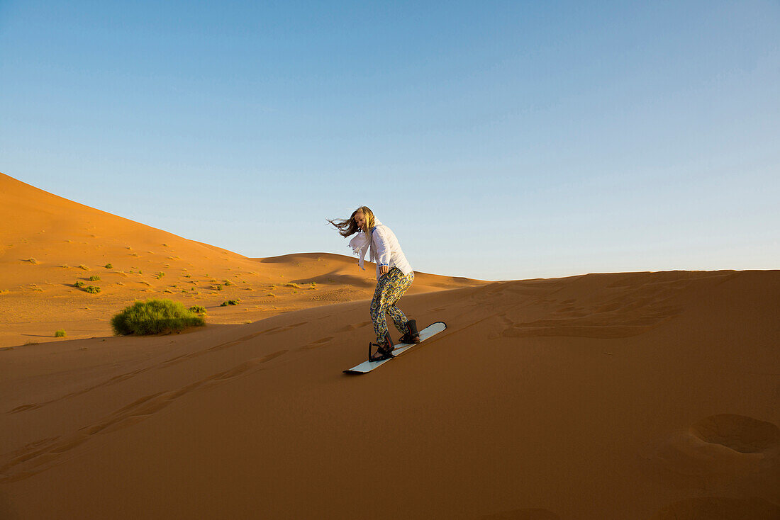 junge Frau mit Snowboard in den Sanddünen bei Merzouga, Erg Chebbi, Sahara, Marokko, Afrika