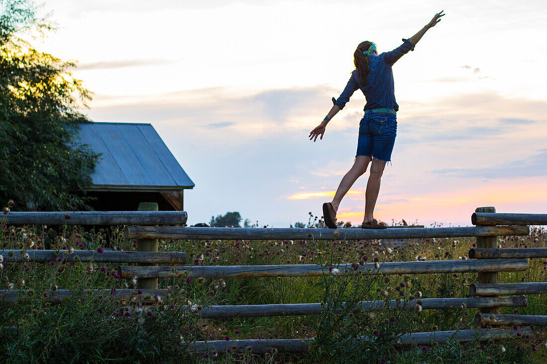 Woman balances on a split rail fence on a ranch in Bozeman, MT in the summertime.