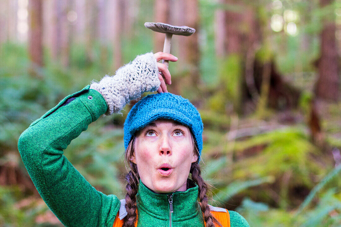 Woman makes a silly face and holds a mushroom on top of her head in the Hoh Rainforest, WA