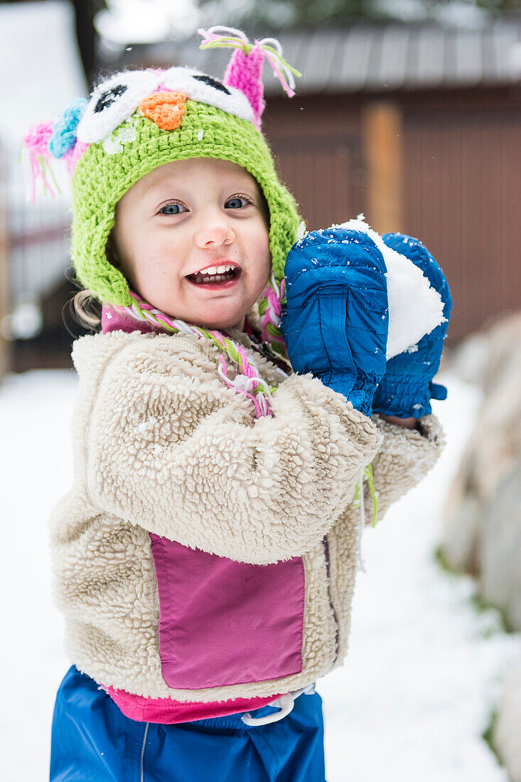 Smiling toddler girl gets ready to throw snowball toward camera, Lake Tahoe, California.