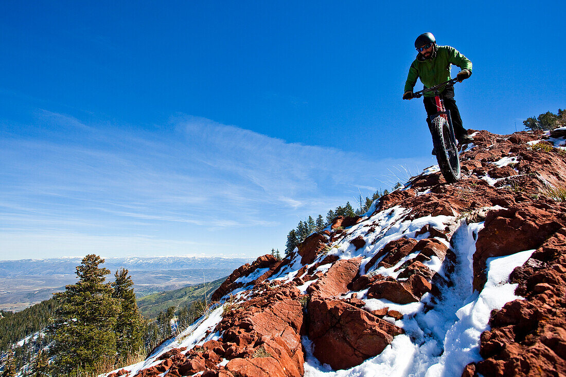 A man rides his fat tire bike along a partially snow covered rocky section of the Crest Trail in Big Cotton Wood Canyon, Utah.