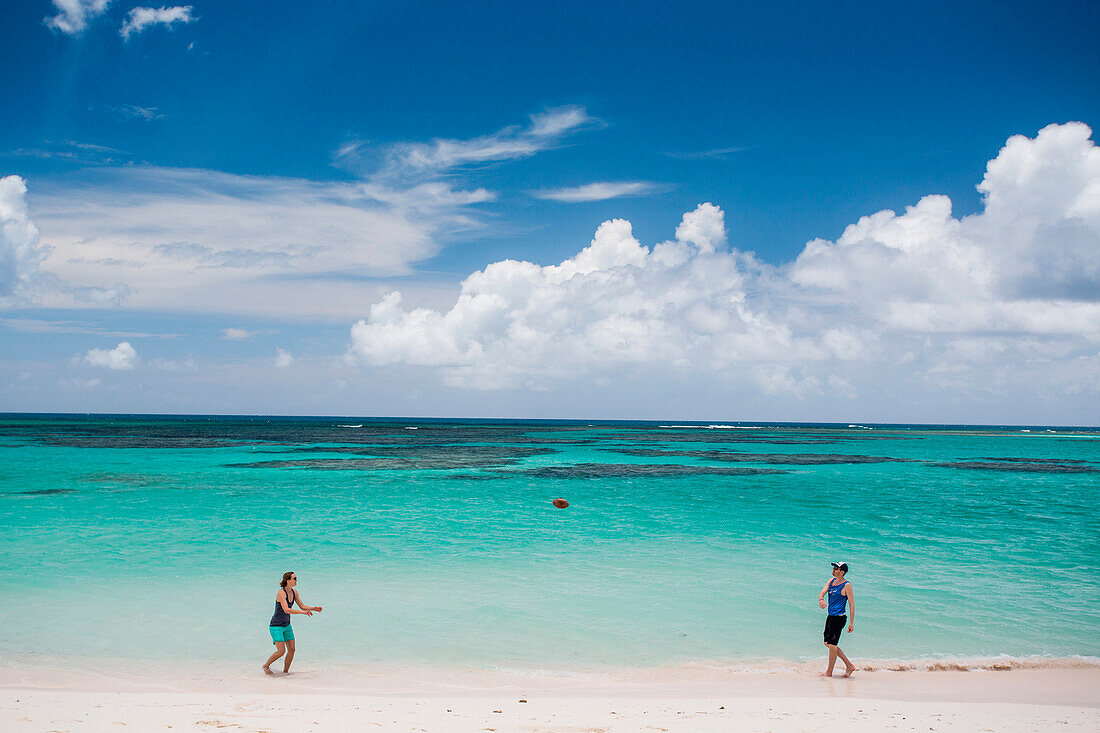 A man and woman throw a football on the white sand beach of the Caribbean's Anegada Island.