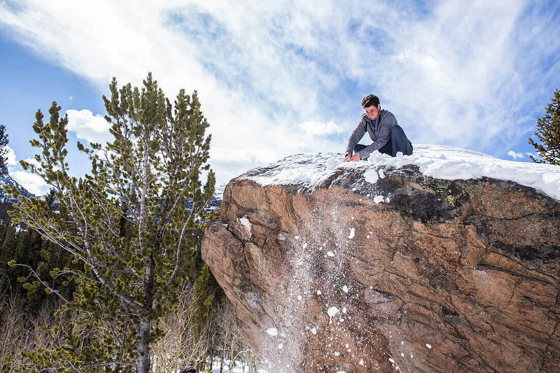 Male climber cleans snow from atop a boulder in Rocky Mountain National Park, Colorado