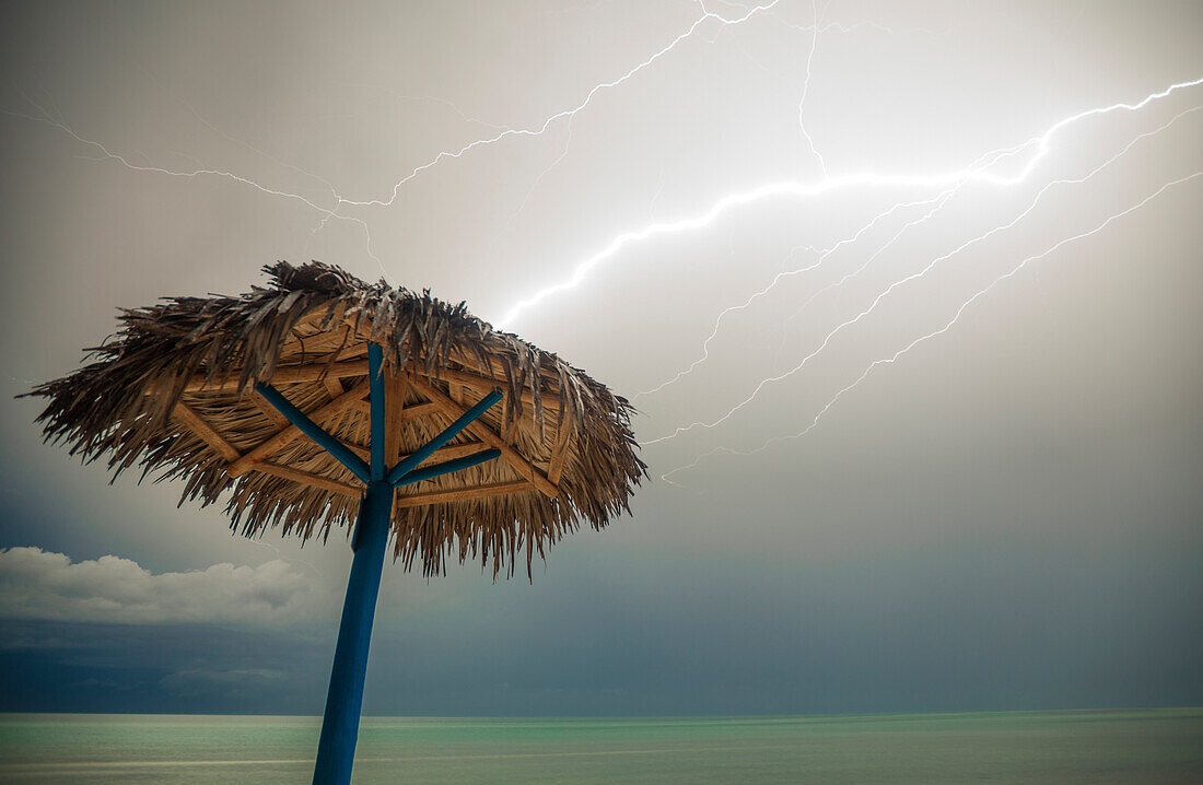 Lightning strikes a beach umbrella made of palm branches on Playa La Jaula beach, Cayo Coco, Cuba.
