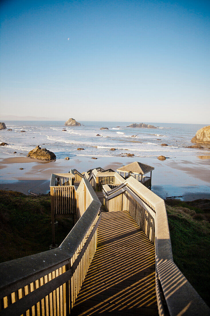 The morning sun shines on a long wooden staircase that leads down to Bandon Bay on the Oregon Coast.