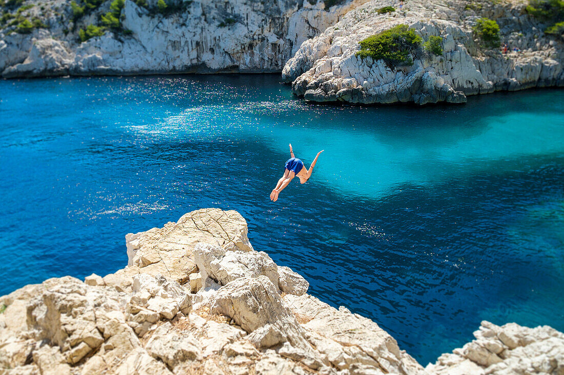 Man diving into beautiful blue water from a rocky outcrop at Calanque de Sugiton, Parc National des Calanques, Provence-Alpes-Côte d'Azur, Bouches-du-Rhône, France