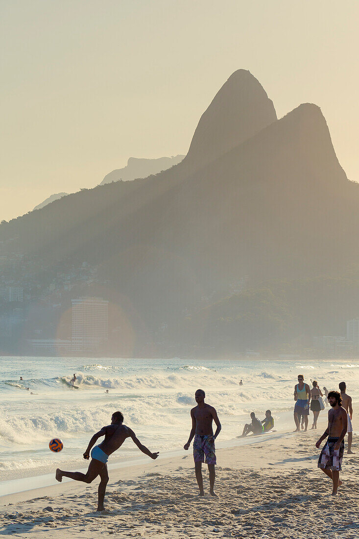 Locals playing football on Ipanema beach with the Morro dos Dois Irmaos (Two Brothers) mountains behind, Rio de Janeiro, Brazil, South America