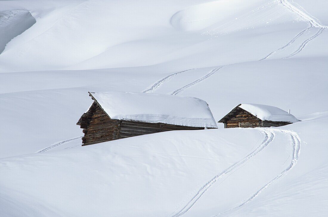 Two old wooden barns surrounded by deep snow and ski tracks in the Dolomites, South Tyrol, Italy, Europe