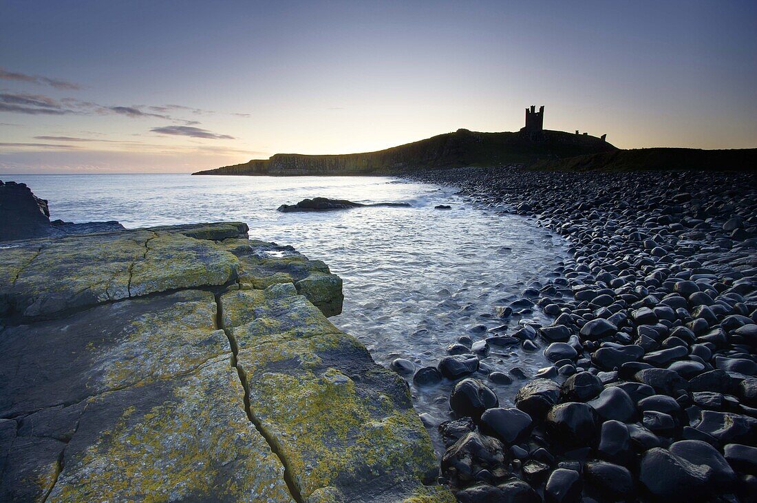 View across the Rumble Churn at dawn towards the ruins of Dunstanburgh Castle, Embleton Bay, near Alnwick, Northumberland, England, United Kingdom, Europe