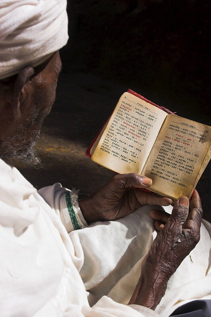 Old man wearing traditional gabi (white shawl) reading Holy Bible in rock-hewn monolithic church of Bet Medhane Alem (Saviour of the World), Lalibela, Ethiopia, Africa